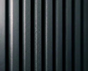 A detailed close-up view of parallel dark charcoal grey fluted wood panels, showing a detailed textured matte finish and deep vertical shadow lines.
